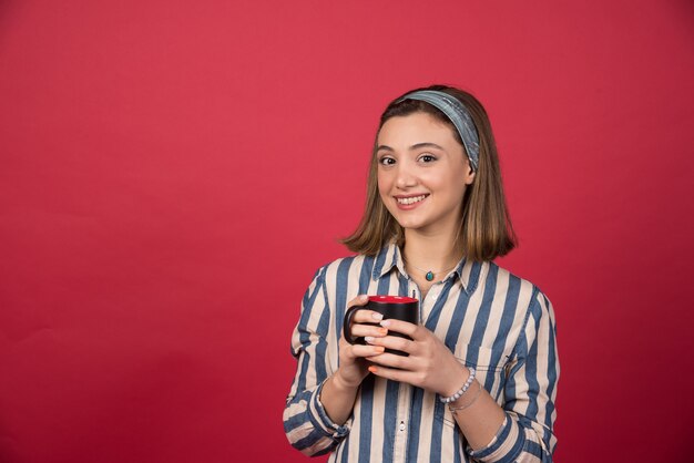 Mujer alegre sosteniendo una taza de café y posando al frente