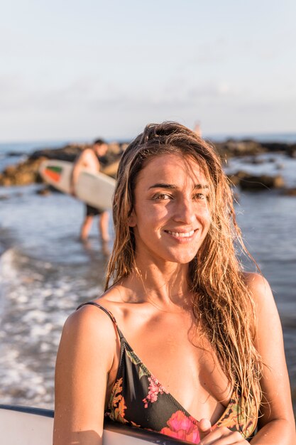Mujer alegre con tabla de surf de pie cerca del mar