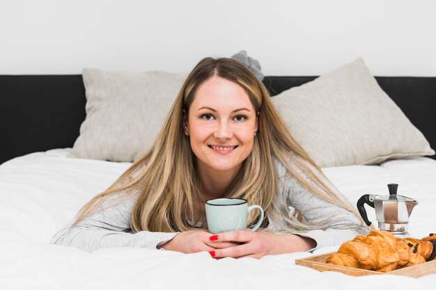 Mujer alegre con taza en la cama