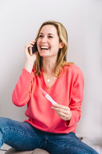 Mujer alegre con test de embarazo haciendo llamada