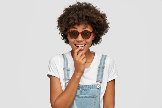 Mujer alegre tiene peinado afro rizado tupido, sonríe positivamente