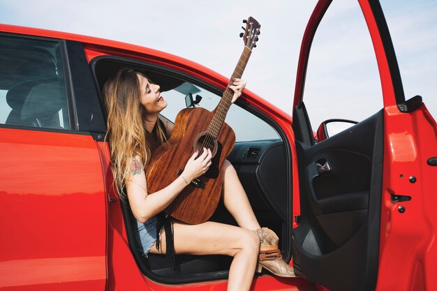 Mujer alegre tocando la guitarra en el coche rojo