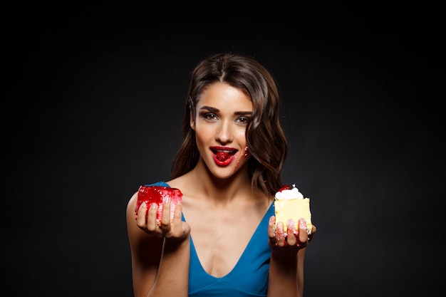 Mujer alegre en vestido azul comiendo dos pedazos de pastel