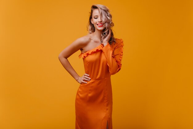 Mujer alegre en vestido largo jugando con su cabello