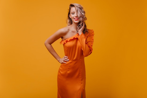 Mujer alegre en vestido largo jugando con su cabello