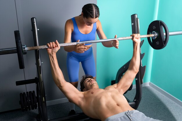 Mujer de alto ángulo ayudando al hombre en el gimnasio