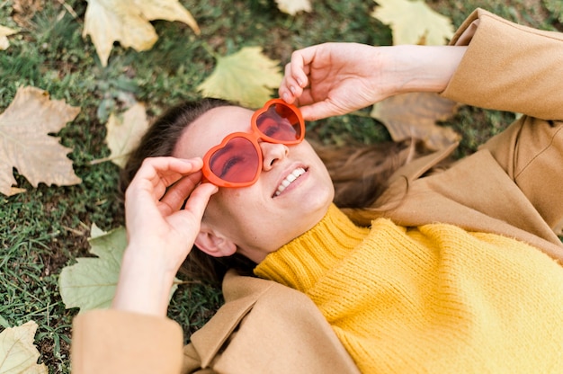 Mujer de alto ángulo con gafas en forma de corazón junto a las hojas de otoño