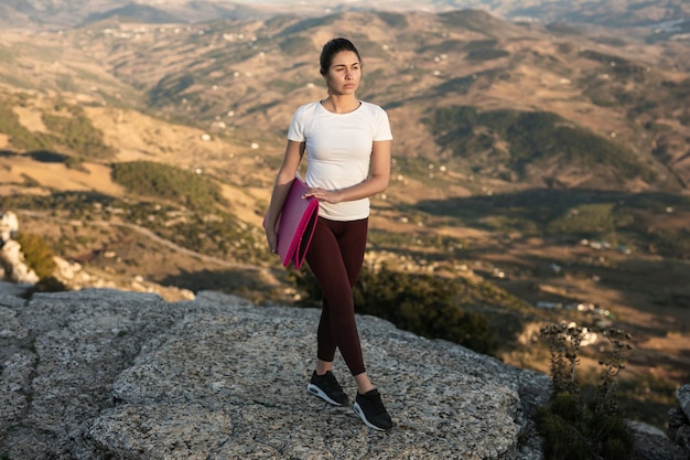 Mujer de alto ángulo en la montaña con colchoneta de yoga