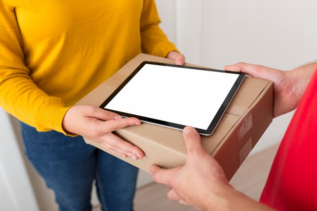 Mujer de alto ángulo y repartidor sosteniendo una caja y una tableta de pantalla vacía