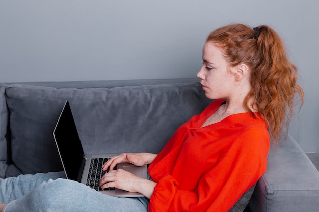 Mujer de alto ángulo en el sofá trabajando en la computadora portátil