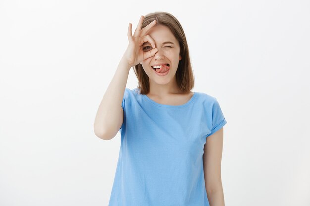 Mujer amable despreocupada riendo feliz y mostrando bien firmar sobre los ojos, todo bien, todo perfecto