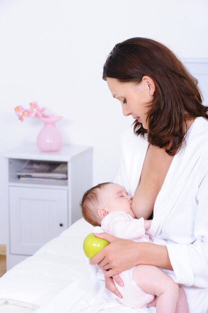 Mujer amamantando a su bebé y sosteniendo apple