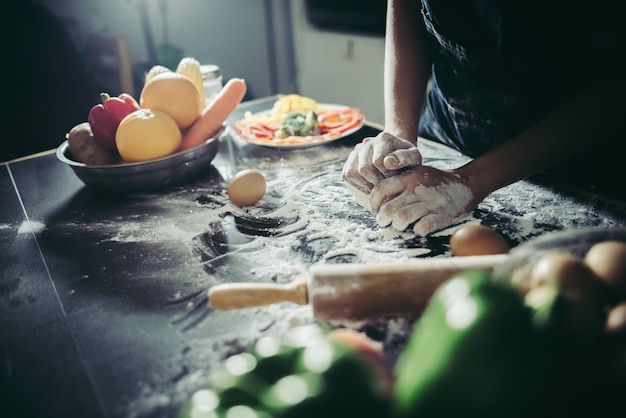 La mujer amasa la pasta para hacer la pizza en de madera. Concepto de cocina