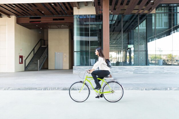 Mujer ambientalista montando bicicleta en la calle contra el edificio de oficinas