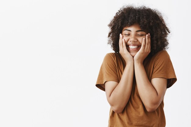 Mujer de américa africana complacida en el amor que siente emoción y afecto siendo elevada y tocada después de una gran cita en un lugar romántico tomados de la mano en la cara cerrando los ojos y sonriendo ampliamente