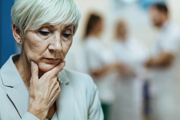 Mujer anciana angustiada sosteniendo la mano en la barbilla y contemplando su enfermedad mientras estaba en la clínica