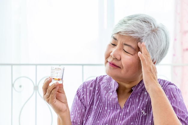 Mujer anciana mayor mirando la taza de vidrio de medición comprobando la medicina sufre de enfermedad