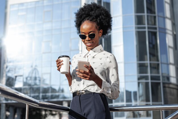 Mujer de ángulo bajo con café mirando móvil