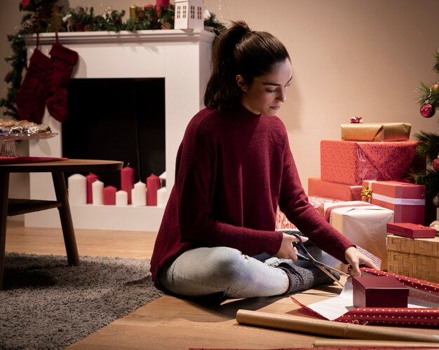 Mujer de ángulo bajo en casa envolviendo regalos