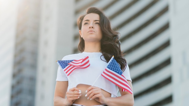 Mujer de ángulo bajo con dos banderas de Estados Unidos