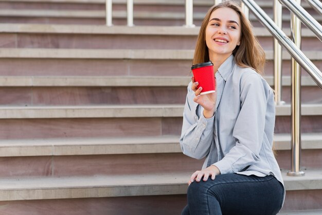 Mujer de ángulo bajo en las escaleras tomando café