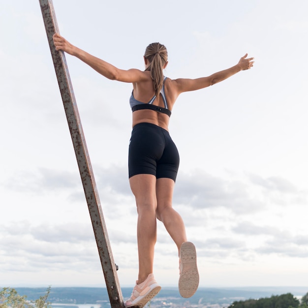 Foto gratuita mujer de ángulo bajo en ropa deportiva sosteniendo ella misma en una barra de metal