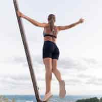 Foto gratuita mujer de ángulo bajo en ropa deportiva sosteniendo ella misma en una barra de metal
