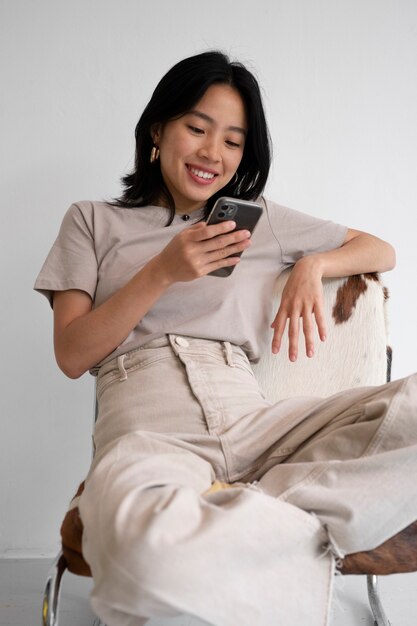 Mujer de ángulo bajo en silla con teléfono inteligente