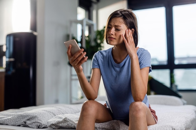 Mujer angustiada con dolor de cabeza mientras lee el mensaje que ha recibido en el teléfono móvil