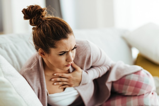 Mujer angustiada sosteniendo su pecho con dolor mientras se acuesta en el sofá de la sala de estar