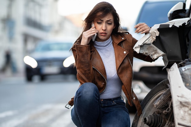 Mujer angustiada usando un teléfono móvil después de un accidente automovilístico y pidiendo ayuda