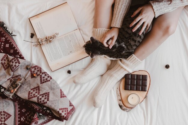 Mujer anónima y gato cerca de libro y chocolate