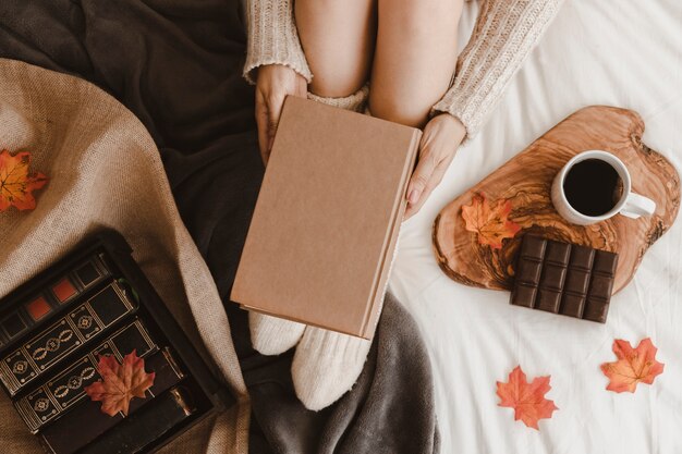 Mujer anónima con libro cerca de té y chocolate