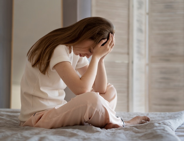 Foto gratuita mujer ansiosa sentada en la cama tiro completo