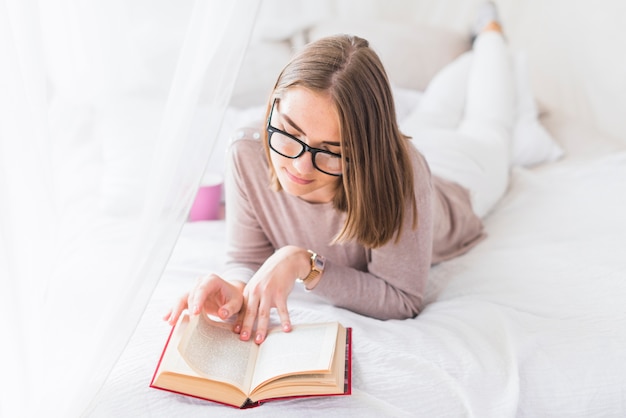 Mujer con anteojos acostado en el libro de lectura de la cama