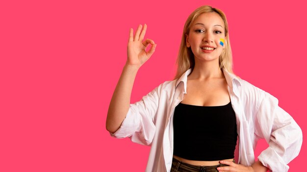 Mujer de apariencia modelo con la bandera de Ucrania en su rostro sostiene posando sobre un fondo rosa