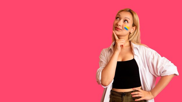 Mujer de apariencia modelo con la bandera de Ucrania en su rostro sostiene posando sobre un fondo rosa