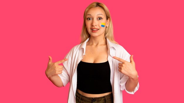 Mujer de apariencia modelo con la bandera de Ucrania en su rostro sostiene posando sobre un fondo rosa