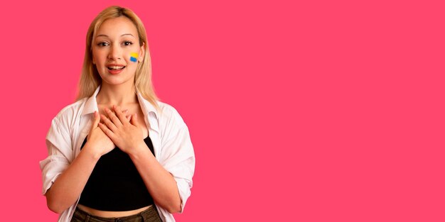 Foto gratuita mujer de apariencia modelo con la bandera de ucrania en su rostro sostiene posando sobre un fondo rosa