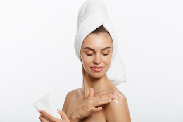 Mujer aplicando crema en el hombro sobre un fondo blanco.