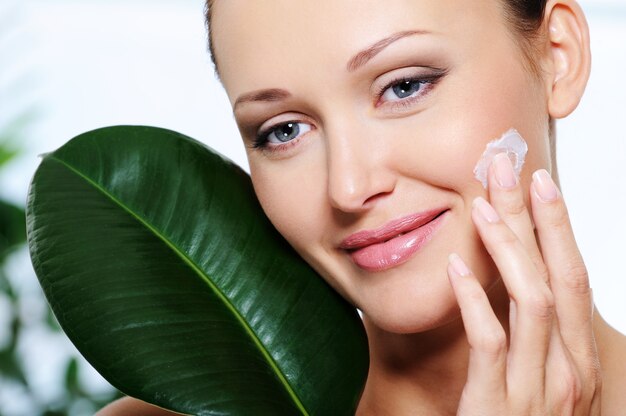 Mujer aplicando crema humectante con una hoja fresca en la cara
