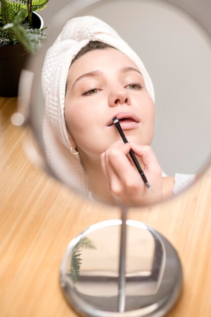 Mujer aplicando lápiz labial en espejo