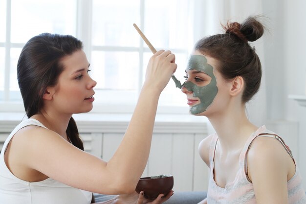 Mujer aplicando una máscara facial a su amiga