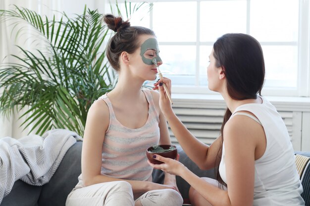 Mujer aplicando una máscara facial a su amiga