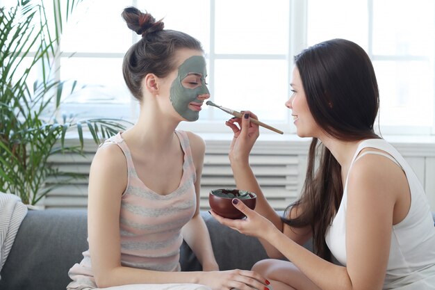 Mujer aplicando una máscara facial a su amiga