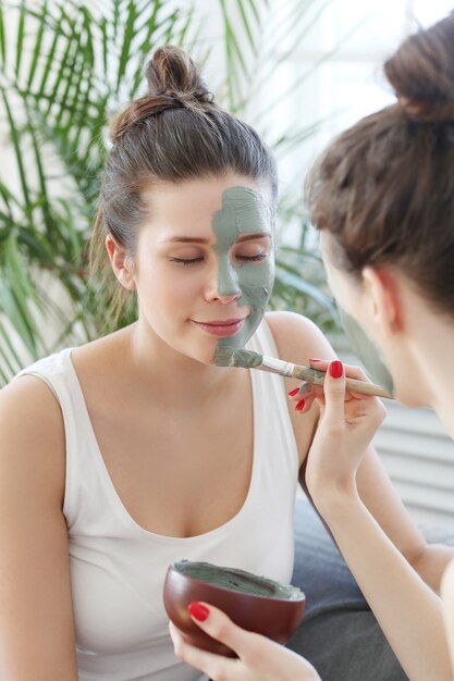 Mujer aplicando una máscara facial a su amiga