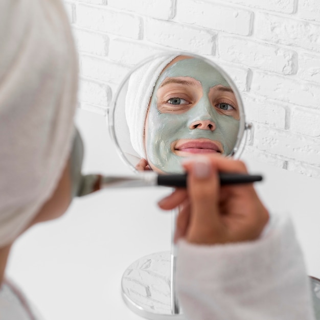 Mujer aplicando remedio facial en el espejo