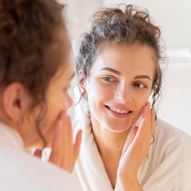 Foto gratuita mujer aplicar crema en la cara mientras mira en el espejo