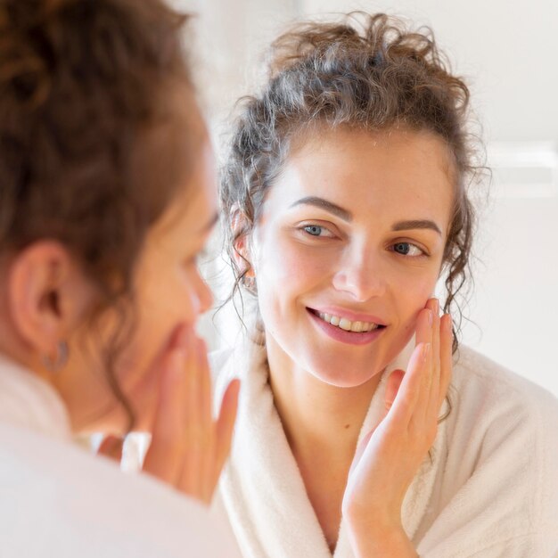 Mujer aplicar crema en la cara mientras mira en el espejo