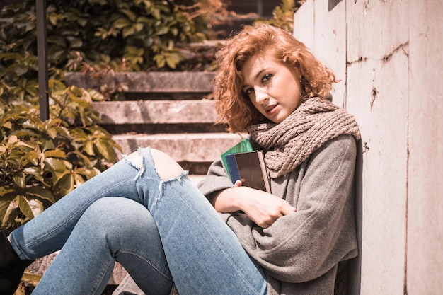 Mujer apoyada en la pared y sosteniendo libros